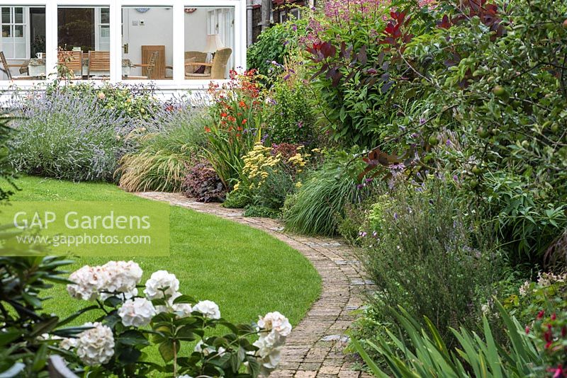 Curving brick path with herbaceous border and lawn