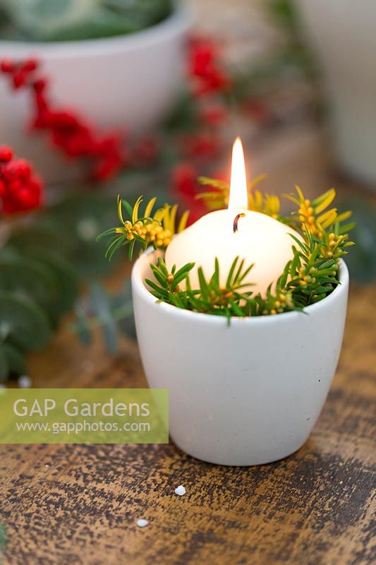 Candle in white pot with foliage decoration.