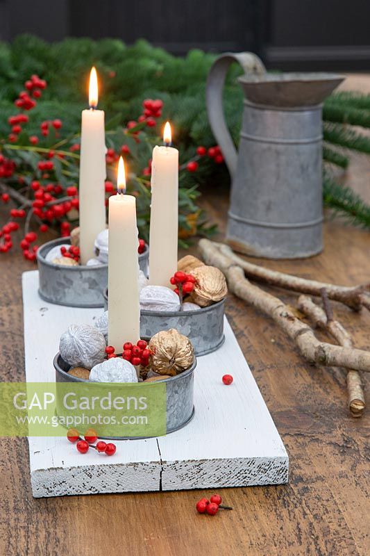 Table centrepiece of candle holders featuring painted walnuts and Ilex berries.