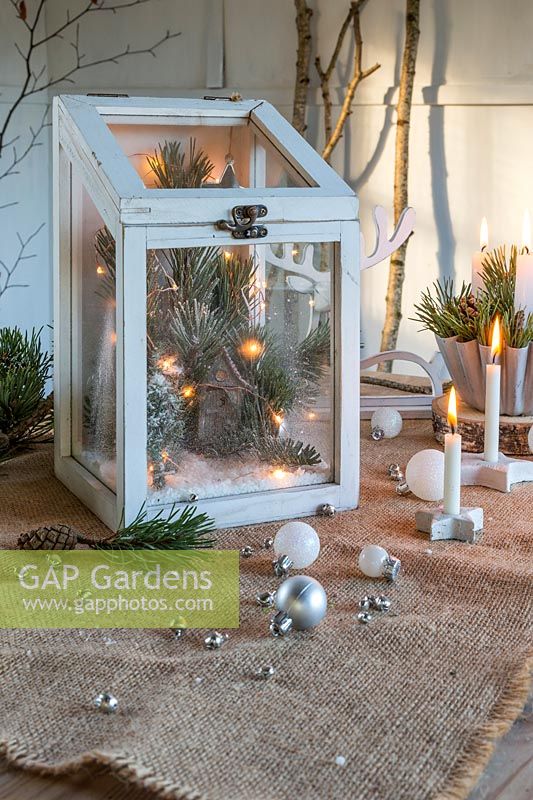 Festive arrangement using pine foliage and cones, LED lights, candles and baubles in rustic setting. 