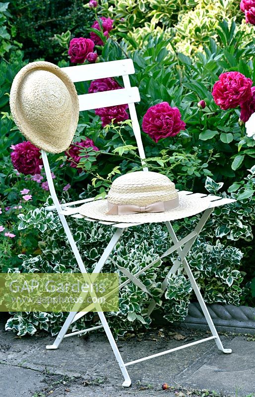 Chair holding vintage straw hats in front of flowering perennial border. 