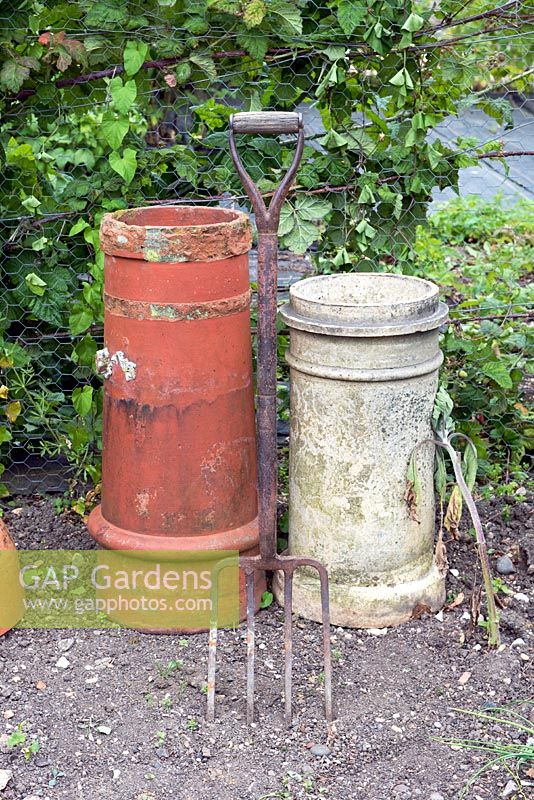 Two Chimney Pots and garden fork in empty border. 