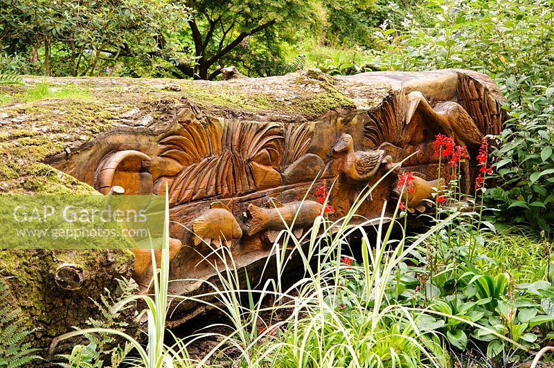 Felled oak carved with seats and scenes of birds, fish and animals by chainsaw sculptor Matthew Crabb. Abbotsbury Subtropical Gardens, Abbotsbury, Dorset, UK. 