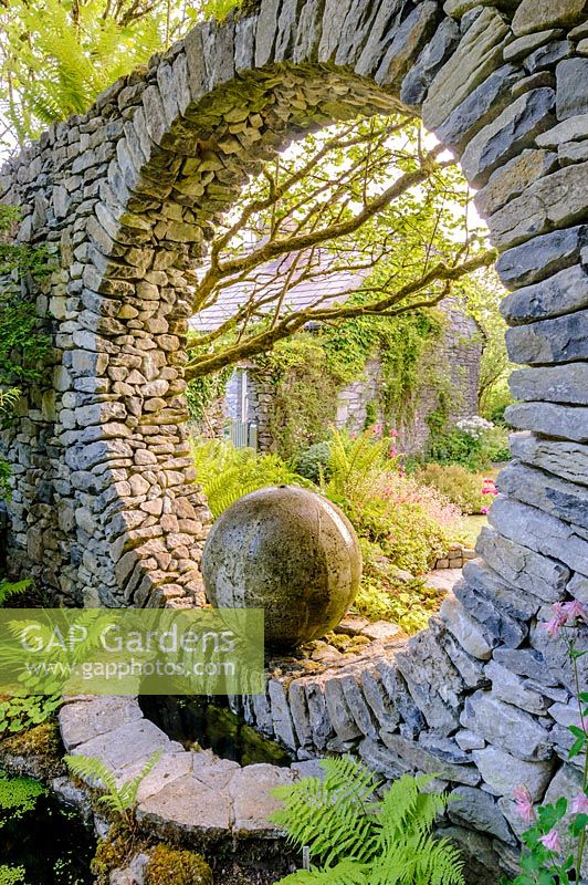 Moon Window in stone wall with cast concrete water feature with shade loving ferns. Fanore, Ireland