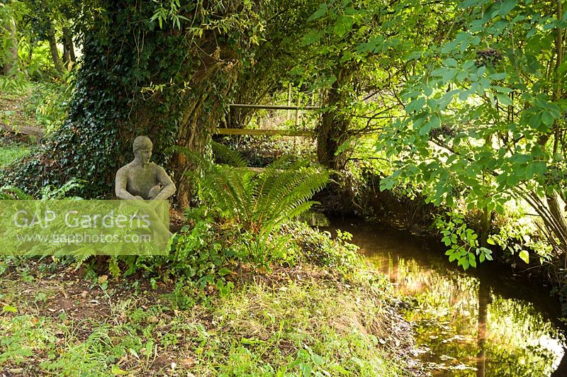 Sculpture of a seated woman beside stream, Aston Crews, Herefordshire, UK.