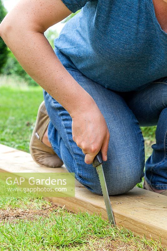 Close up detail of woman using a kitchen knife and wooden guide to trim turf to correct size