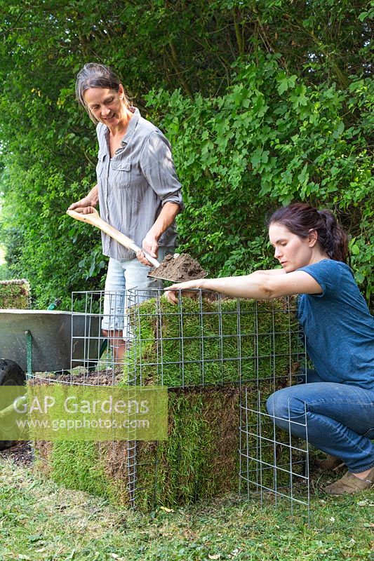 Women working together to backfill topsoil into a gabion lined with turf