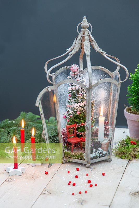 Christmas scene of miniature tree, chair and lit candle in metal lantern