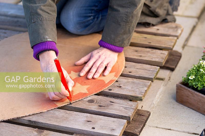Woman using a cardboard template to mark a heart shape on pallet