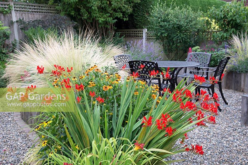 View of flowering summer border to garden table and chairs. 

