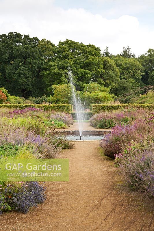 Fountain on gravel paths with mixed perennials, Scampston Hall, North Yorkshire, UK
