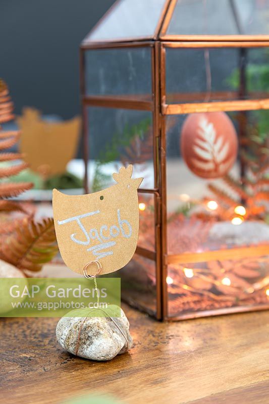 Copper themed Easter display in copper lantern with place names made from chicken shaped name cards fixed to pebble with copper wire