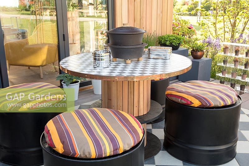 Repurposed wooden table with oil drum seats and cushions. 'At Home - Grow, Dine, Relax' garden, RHS Malvern Spring Festival, 2018.