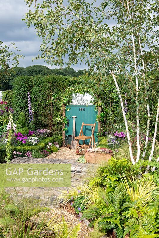 Chair next to a green garden gate with tools, brick patio and Betula underplanted with native ferns - 130 Years of Port Sunlight, The Garden Village, RHS Tatton Park Flower Show 2018