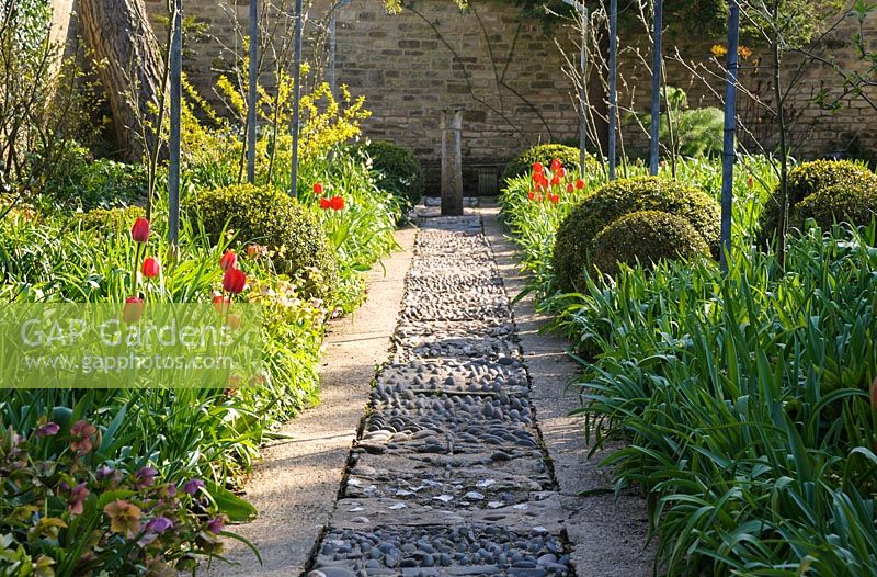 Pebble mosaic path with red tulips 'Apeldoorn' in adjoining beds at Barnsley House, Cirencester, UK