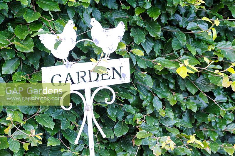 Decorative cut metal garden sign against a beech hedge.