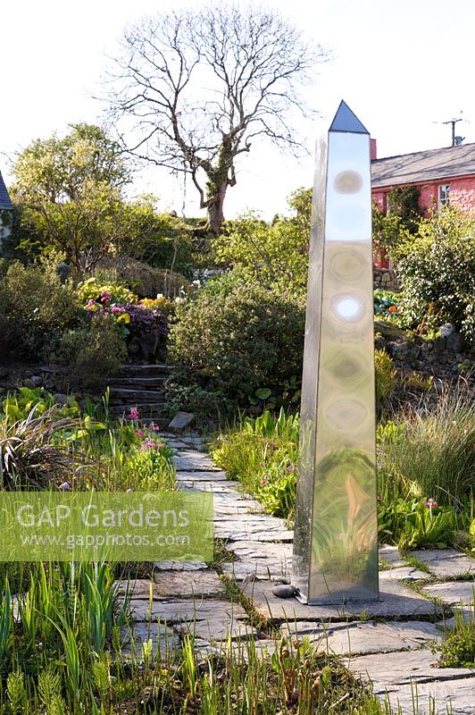 Stainless steel obelisk in the bog garden surrounded by the new leaves of Gunnera manicata.