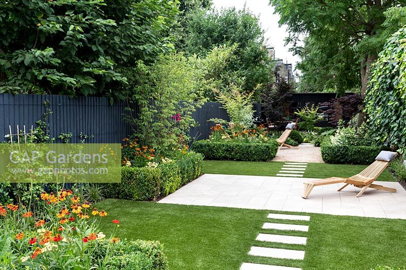 Garden design by Nick Gough 
Overview of garden with artificial lawn with stone slab path and patio with 
wooden chairs. Planting on the left: buxus sempervirens hedge 
Orange Helenium 'Moerheim Beauty' 
Yellow Achillea 'Teracotta'  
Pink Cirisium riv. Altropurpureum
