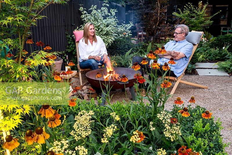Owners Claire and Sean McHugh sitting in garden with Helenium 'Moerheim Beauty'and Achillea