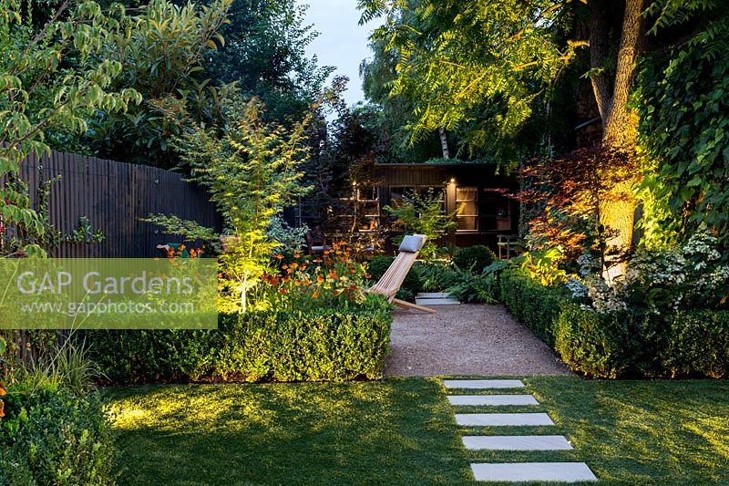 Illuminated borders with path on artificial lawn and Buxus sempervirens hedge 