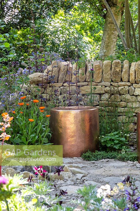 Copper seating surrounded by a dry stone wall. The Warner Edwards Garden, a representation of Falls Farm in the Northamptonshire countryside, Sponser: Warner Edwards, RHS Chelsea Flower Show, 2018.

