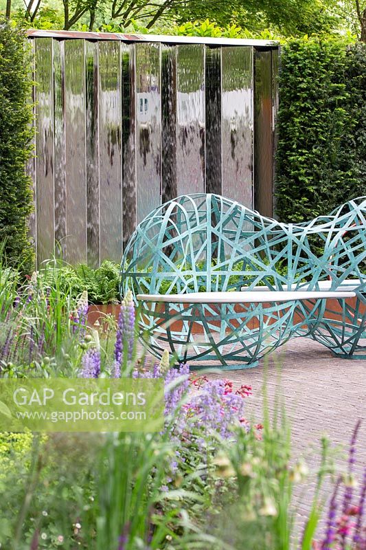 Blue sculptural benches surrounded by metal screens and perennial planting - The David Harber and Savills garden, Sponsor: David Harber and Savills. RHS Chelsea Flower Show, 2018.