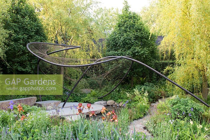 Metal sculpture over natural stone paving and pool with Salix alba 'Tristis' and Iris 'Carnival Time' - The Wedgwood Garden - RHS Chelsea Flower Show 2018