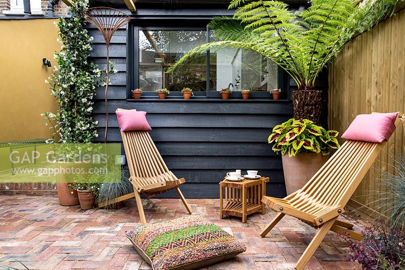 Pair of wooden garden chairs in London patio garden. 
