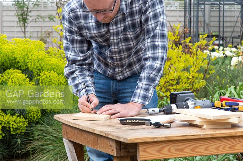 Man using a ruler to measure and mark hole in wood. 