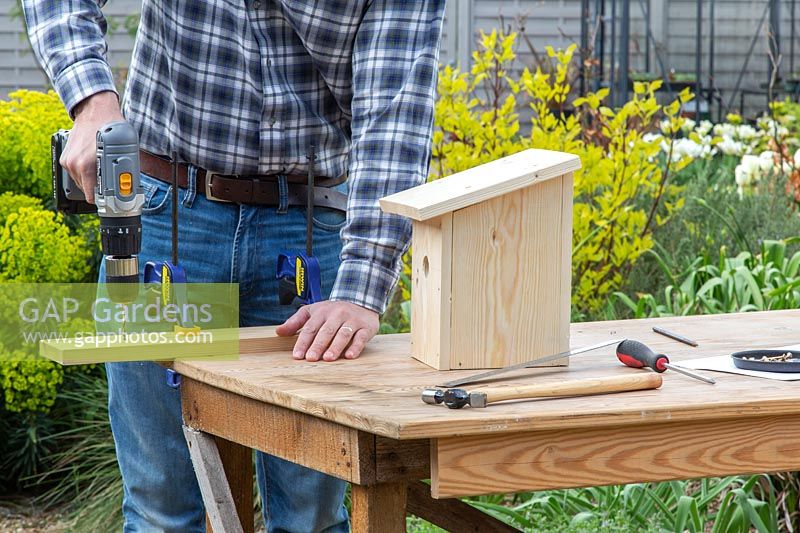 Man using drill to make holes in piece of wood used for back board. 