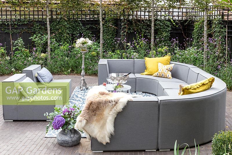 Grey outdoor sofa arrangement with yellow cushions, fleece,  tables, drinks and floral arrangements. 