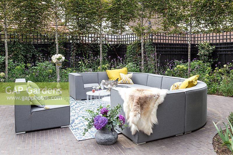 Grey outdoor sofa arrangement with yellow cushions, fleece,  tables, drinks and floral arrangements. 