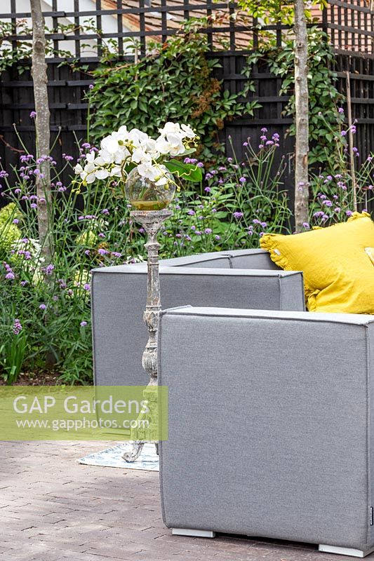 Grey outdoor sofa arrangement with yellow cushions and floral arrangement