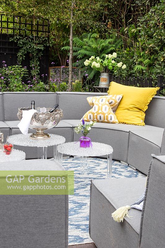 Grey outdoor sofa arrangement with yellow cushions, tables, drinks and rug
