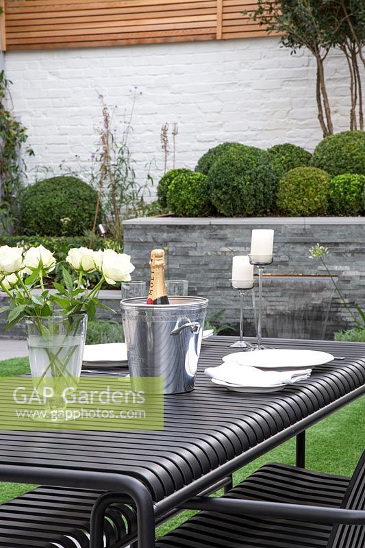 Outdoor table set with white roses, candles and champagne bottle in cooler