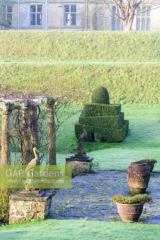 Stone crane statues in the Fountain Court, with clipped Buxus and Taxus, and decorative urns at Mapperton, Dorset. 