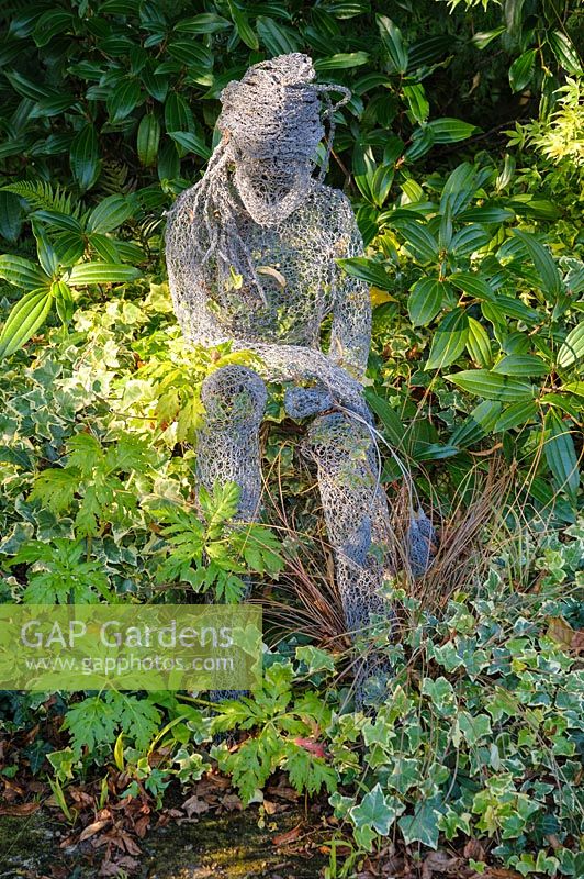 Sculpture of seated female figure by Derek Kinzett surrounded by foliage plants - Shropshire, UK