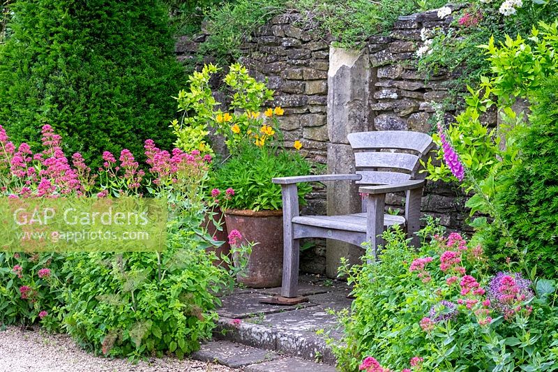 View of wooden chair surrounded by flowering plants, Hanham Court Gardens, Bristol, UK. 