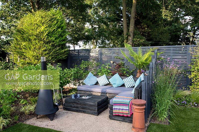 Contemporary London garden with grey painted fence. Wooden post screen - Lower seating area with Chimenea Purple flower is Verbena bonariensis Tree Fern  - Dicksonia Antarctica