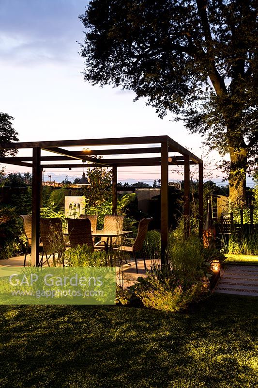 Contemporary London garden in late evening with artificial light looking 
towards pergola and patio eating area