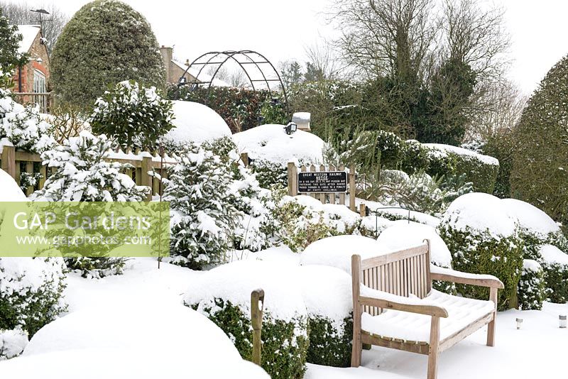 The sloping garden with evergreens such as clipped Box, Yew and Bay providing structure in the snow, wooden bench which looks out over the Blackmore Vale.