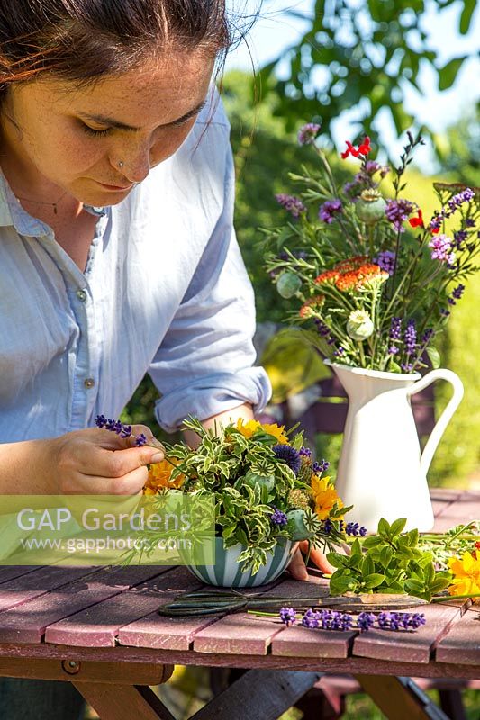 Woman creating floral arrangement in bowl using garden flowers 