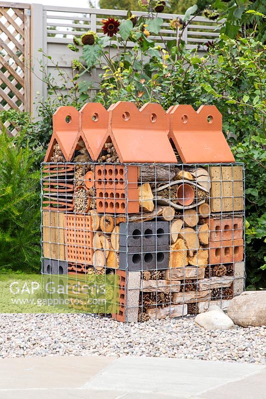 Insect hotel in wire gabion with building materials and dried plants