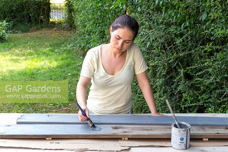 Woman painting the long boards grey using a paint brush