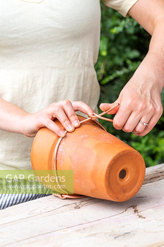 Twisting copper wire around a terracotta pot to enable the pot to hang from the wire loop