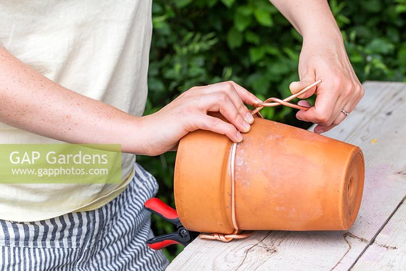 Twisting copper wire around a terracotta pot to enable the pot to hang from the wire loop