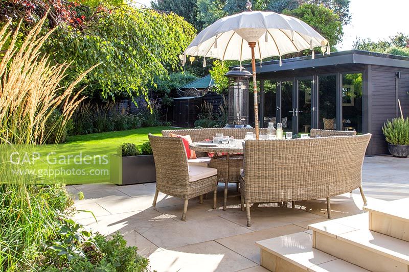 Dining furniture with umbrella on modern patio with view to Summerhouse. 