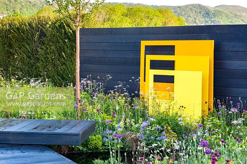 Yellow steel sculptural panels with black fence and meadow-style planting. 'Urban Oasis', RHS Malvern Spring Festival 2018.