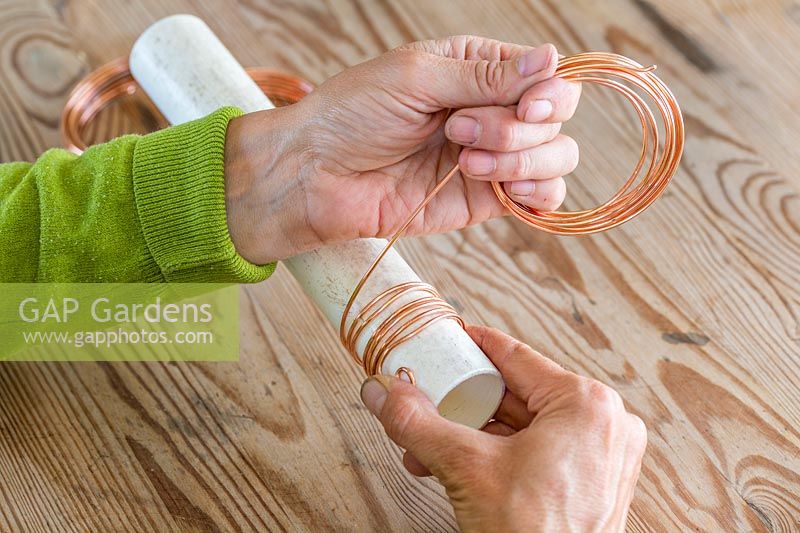 Person winding copper wire around plastic tube to create coiled spring. 