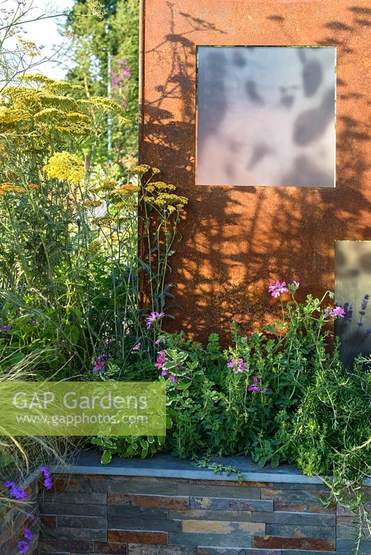 Stone veneered raised bed and COR-TEN steel screen with Achillea and   Pelargonium. 'RNIB Community Garden', RHS Hampton Flower Show 2018.